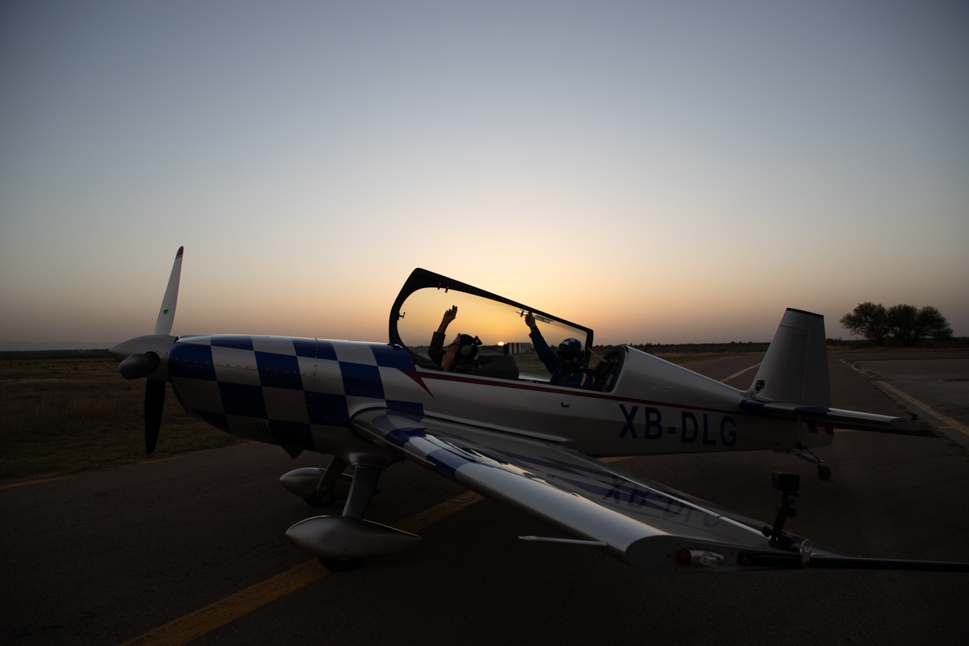 Extra 330 XB-DLG on the strip with canopy up, both pilots waving at sunset